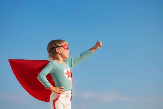 Enfant de super-héros jouant en plein air Enfant de super-héros sur fond bleu ciel d'été Concept d'imagination et de liberté