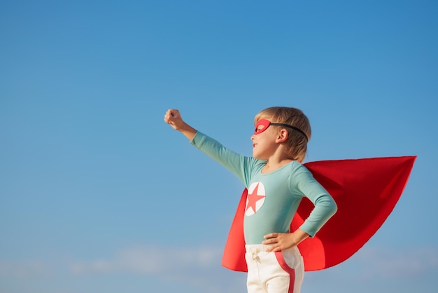 Enfant de super-héros jouant en plein air Enfant de super-héros sur fond bleu ciel d'été Concept d'imagination et de liberté