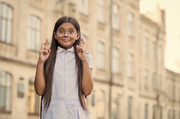 Un enfant superstitieux aux cheveux longs dans des lunettes fait un vœu en croisant les doigts pour l'espace de copie de la superstition de la chance