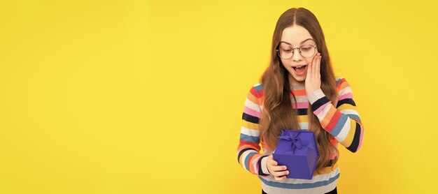 Un enfant surpris dans des lunettes tient une boîte-cadeau pour une surprise d'anniversaire d'anniversaire Enfant avec une affiche horizontale de cadeau d'anniversaire En-tête de bannière avec espace de copie
