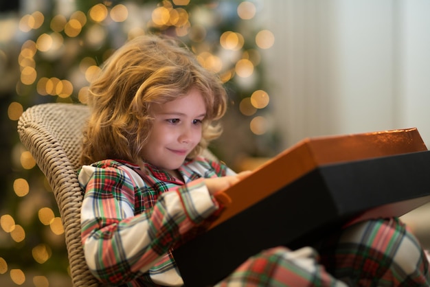Enfant surprise ouvrant la magie de Noël présente un enfant heureux près de l'arbre de Noël à la maison