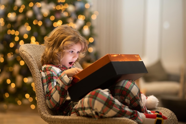 Enfant surprise ouvrant la magie de noël présente un enfant heureux près de l'arbre de noël à la maison