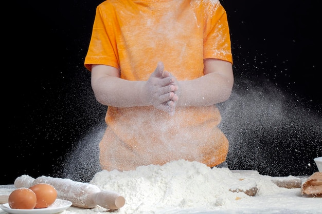 Un enfant en T-shirt orange joue avec de la farine dans la cuisine