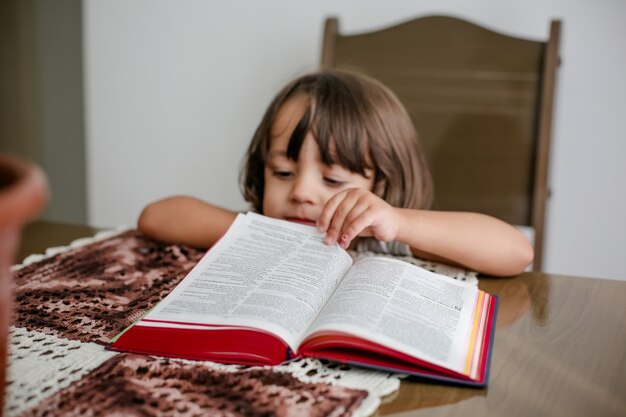 Enfant sur la table lisant la sainte bible et la feuilletant