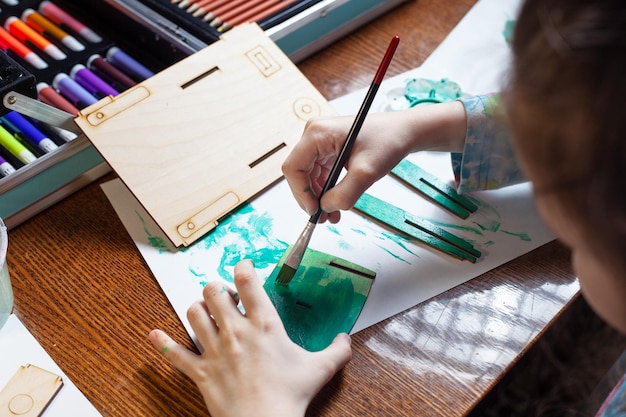 Un enfant sur une table peint des pièces en bois avec de la peinture verte