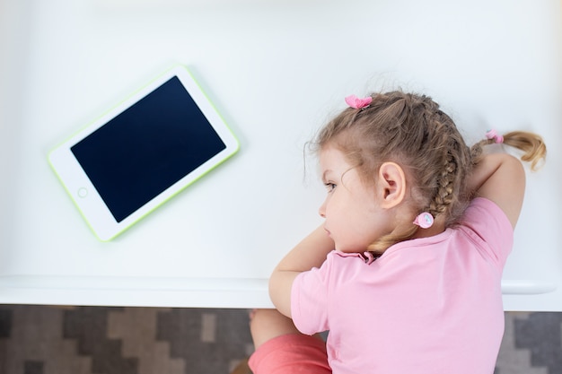 Photo un enfant avec une tablette blanche. kid sur l'éducation en ligne, e-learning tout en quarantaine. kid regarde des dessins animés sur tablette.