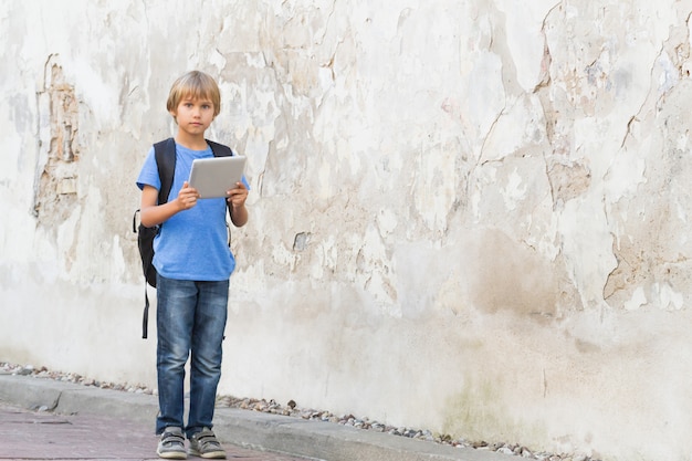 Enfant avec tablette numérique et sac à dos dans la rue de la ville