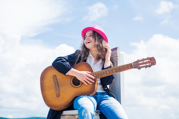 Enfant talentueux style musique country instrument de musique à cordes jouer à la guitare acoustique petite fille jouer de la guitare elle aime la musique cours d'école de musique petit joueur de guitare sur fond de ciel