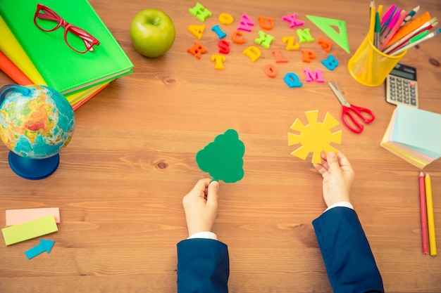 Enfant tenant un arbre à papier et du soleil dans les mains Articles scolaires sur un bureau en bois en classe Concept d'éducation