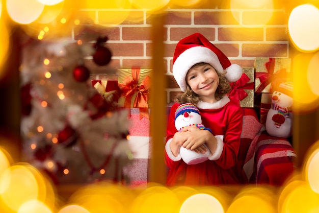 Enfant tenant un bonhomme de neige à côté de l'arbre de Noël