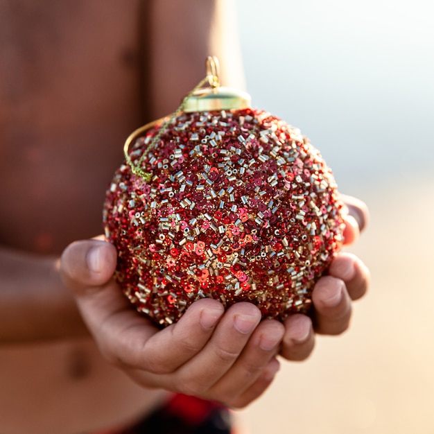 Enfant tenant une boule de Noël rouge au coucher du soleil de Noël, concept de vacances de saison