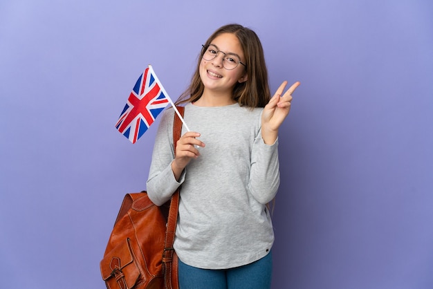 Enfant tenant un drapeau du Royaume-Uni sur fond isolé souriant et montrant le signe de la victoire