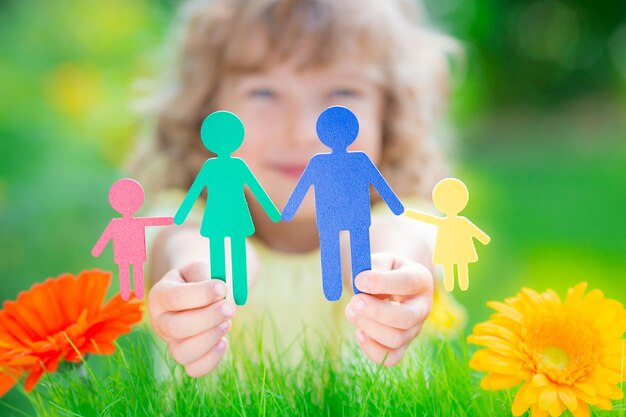 Photo enfant tenant une famille de papier multiethnique dans les mains sur fond vert printemps