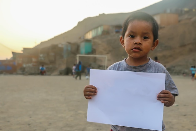 Enfant tenant une feuille de papier vierge pour insérer un texte ou un message positif ou motivant.