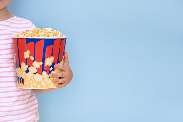 Enfant tenant une grande tasse de papier avec du pop-corn sur fond bleu avec espace de copie