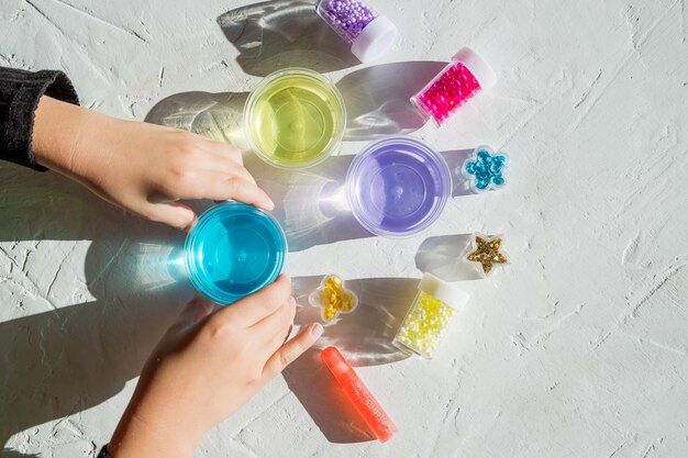 Enfant tenant des ingrédients, des bouteilles, des pots pour fabriquer un jouet populaire pour enfants à partir de colle.