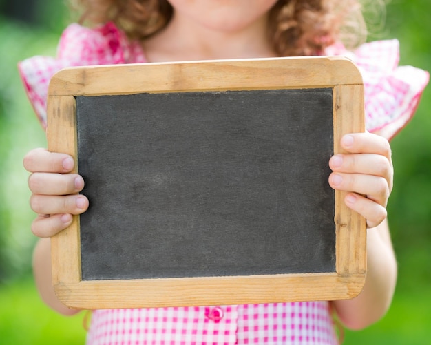 Photo enfant tenant un tableau blanc à l'extérieur