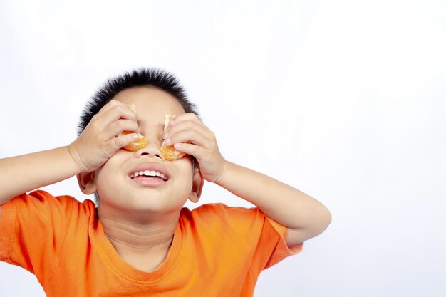 Enfant en tenue orange manger orange isolé sur fond blanc