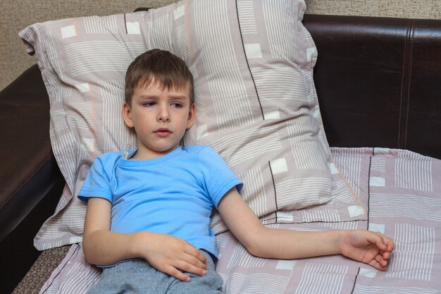 Un enfant avec un thermomètre mesure la température en étant allongé sur le lit. Enfant malade.