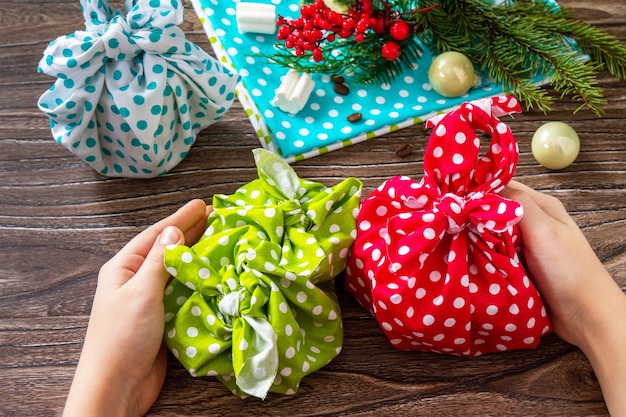 L'enfant Tient Des Cadeaux De Noël Nouvel An Et Emballage Cadeau Furoshiki Zéro Déchet Sur Table En Bois