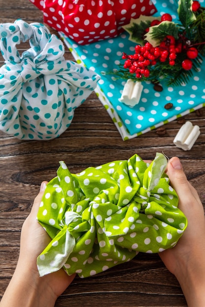 L'enfant tient des cadeaux de Noël Nouvel an et emballage cadeau furoshiki zéro déchet sur table en bois