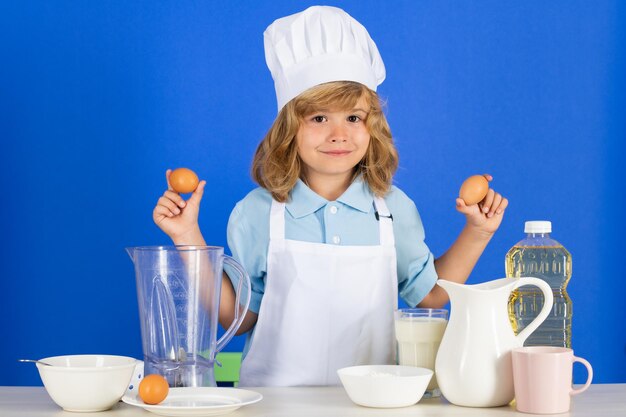 Un enfant tient des œufs portant un uniforme de cuisinière et une toque de chef préparant des légumes sur un portrait de studio de cuisine