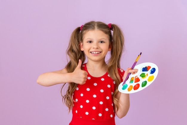 L'enfant tient une palette de peinture et lève le pouce.