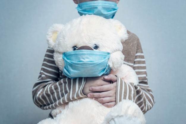 Un enfant tient son ours en peluche tous deux portant des masques médicaux de protection