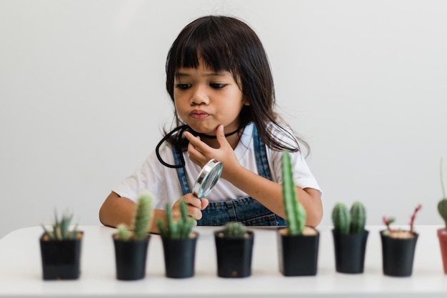L'enfant touche doucement la nouvelle tige du cactus qu'il grandit avec soin une main tient une loupeÉducation à la nature Montessori et concept de compétences d'observation