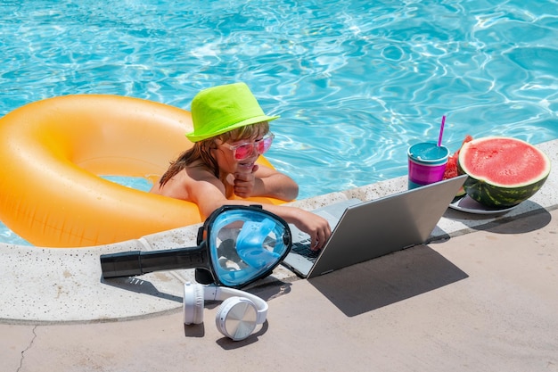 Enfant travaillant avec un ordinateur portable pendant les vacances d'été Petit pigiste utilisant un ordinateur travaillant à distance dans la piscine Technologie en ligne d'été