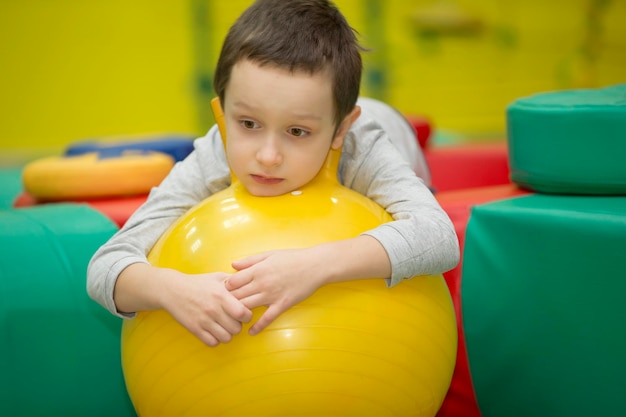 Enfant triste dans la salle de gym. Garçon sur un ballon de gymnastique en caoutchouc