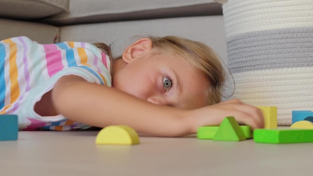 Photo un enfant triste, fatigué, frustré, ennuyé et stressé est allongé sur le sol avec des blocs de bois colorés.
