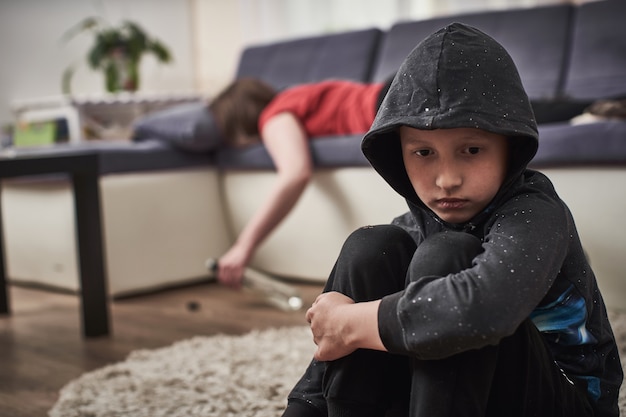 Enfant triste avec mère alcoolique avec une bouteille dans ses mains