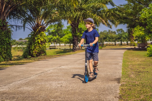 Enfant sur trottinette dans le parc les enfants apprennent à patiner à roulettes petit garçon patinant sur l'été ensoleillé