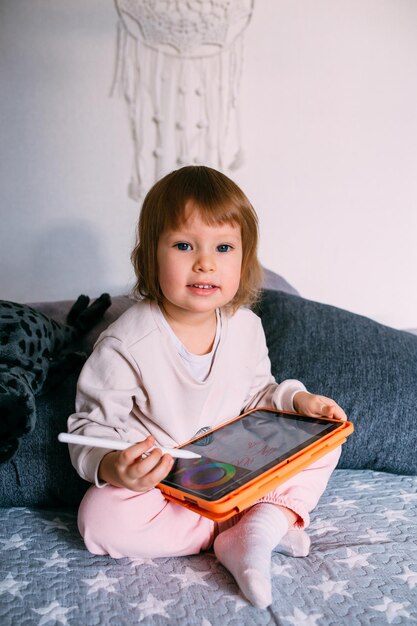 Enfant utilisant la technologie tout-petit à la maison avec une tablette et un stylet et dessine