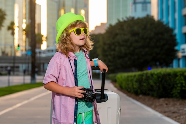 Enfant avec valise partant en vacances Garçon touristique en voyage de vacances enfants concept Joli garçon avec valise sur fond de rue de la ville