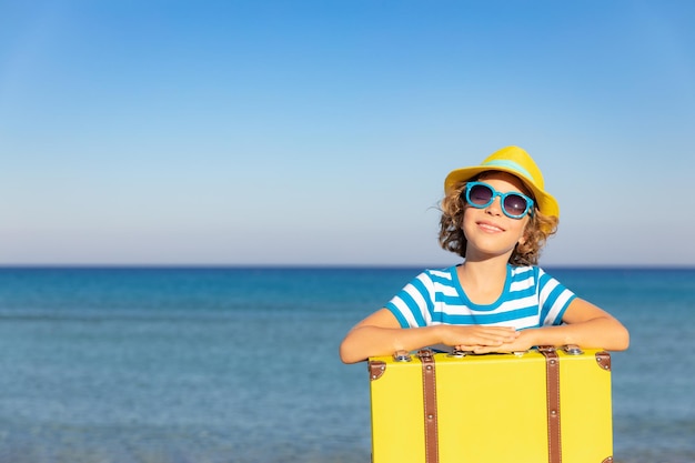 Enfant avec valise vintage en vacances d'été Fille s'amusant sur la plage Enfant assis sur fond de mer et de ciel Concept de voyage et d'aventure