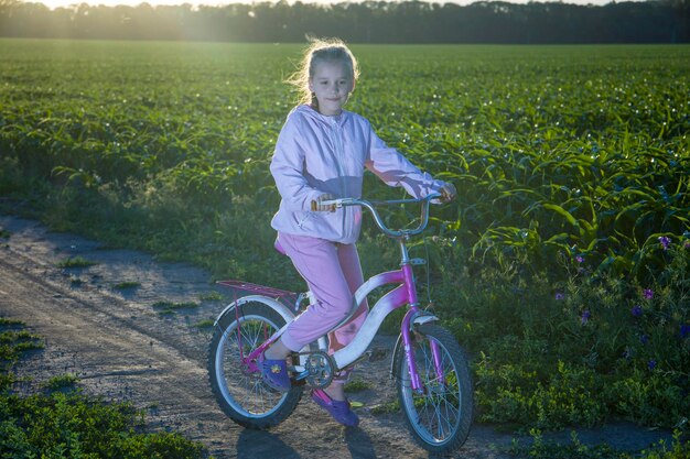 Enfant sur un vélo sur fond de champ vert et avec les rayons du soleil du soir