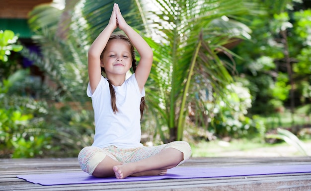 Enfant de yoga faisant des exercices de remise en forme sur la plate-forme de plage à l'extérieur.