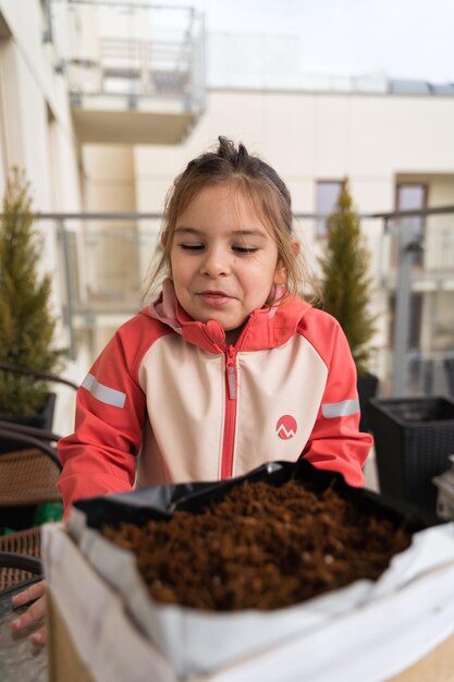 Photo enfante d'âge préscolaire semant des plantes sur le balcon jardinage urbain éducation durable