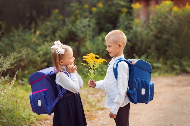 Photo enfants de 7 à 8 ans, élèves du primaire avec des sacs à dos et des uniformes scolaires, un garçon donne des fleurs à une fille