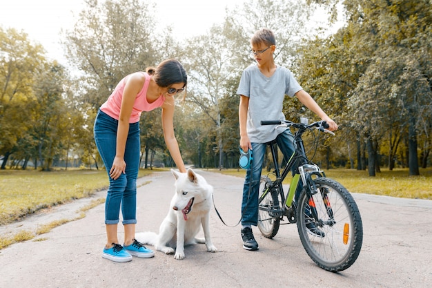 Enfants adolescents sur la route dans le parc avec chien blanc Husky