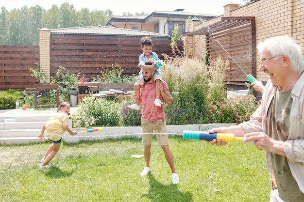 Enfants et adultes passent du bon temps dans l'arrière-cour à tirer des pistolets à eau