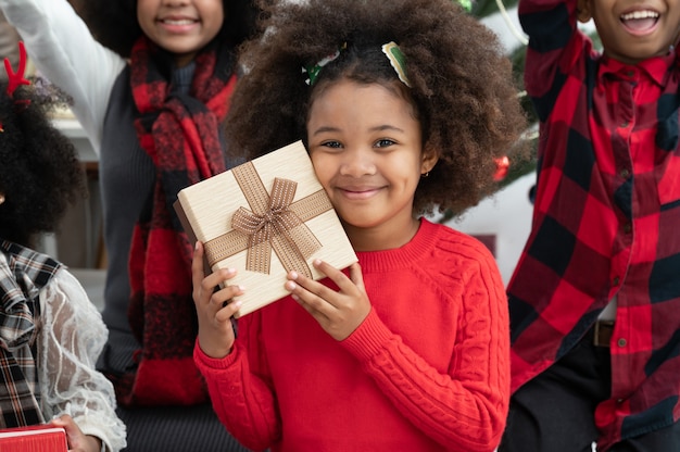 Des enfants afro-américains afro-américains heureux posent dans une pièce avec une boîte-cadeau et des décorations de Noël