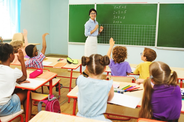 Les enfants d'âge préscolaire lèvent les mains pour répondre à la question de l'enseignant, la classe à l'école primaire.