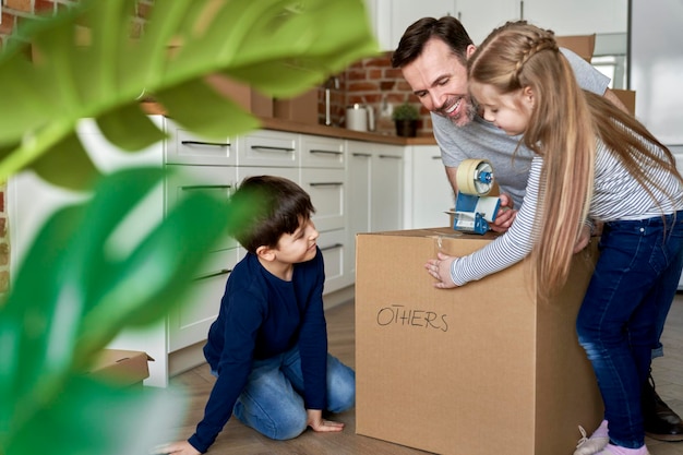 Les enfants aident leur père à emballer des boîtes de carton pour le déménagement