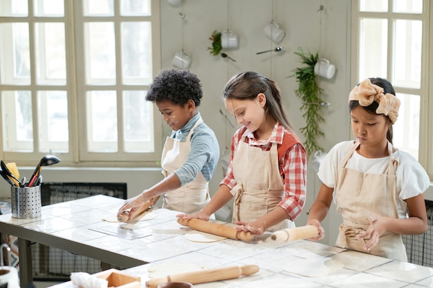 Enfants apprenant à rouler la pâte à table