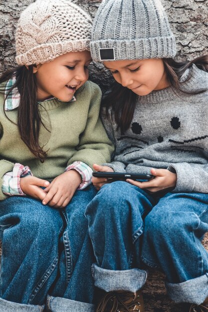 Les enfants en arrière-plan des journaux jouent avec un smartphone. Regardez la vidéo et amusez-vous. Amitié, sœurs, famille.