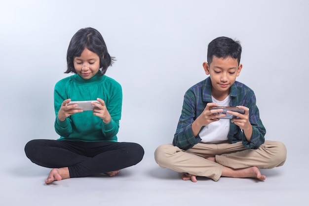 Des enfants asiatiques assis sur le sol jouant à des jeux vidéo compétitifs sur leur smartphone.