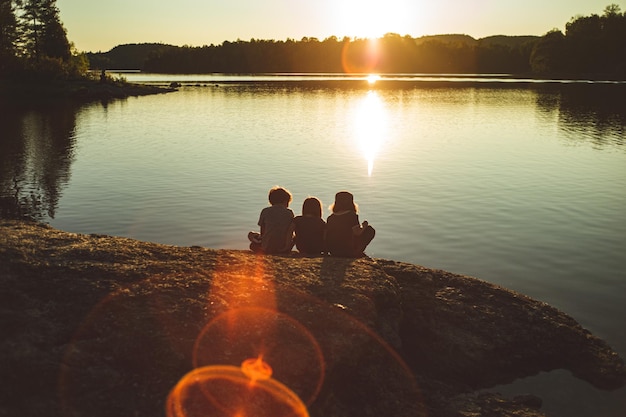 Photo des enfants assis au bord du lac contre le ciel au coucher du soleil